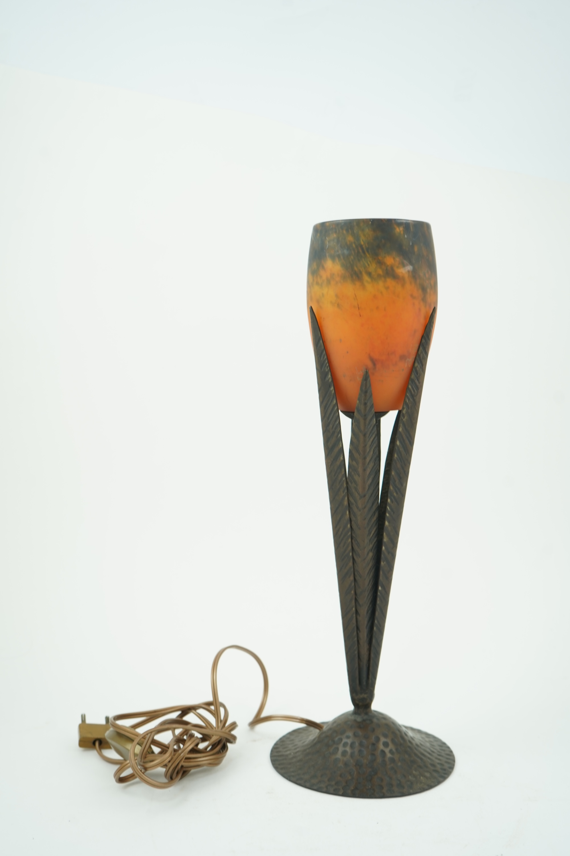 Manner of Muller Freres and Robj: A French Art Deco table lamp the mottled orange glass shade supported by naturalistic palm-leaf metal supports terminating in a circular hammered metal base, 40cm high